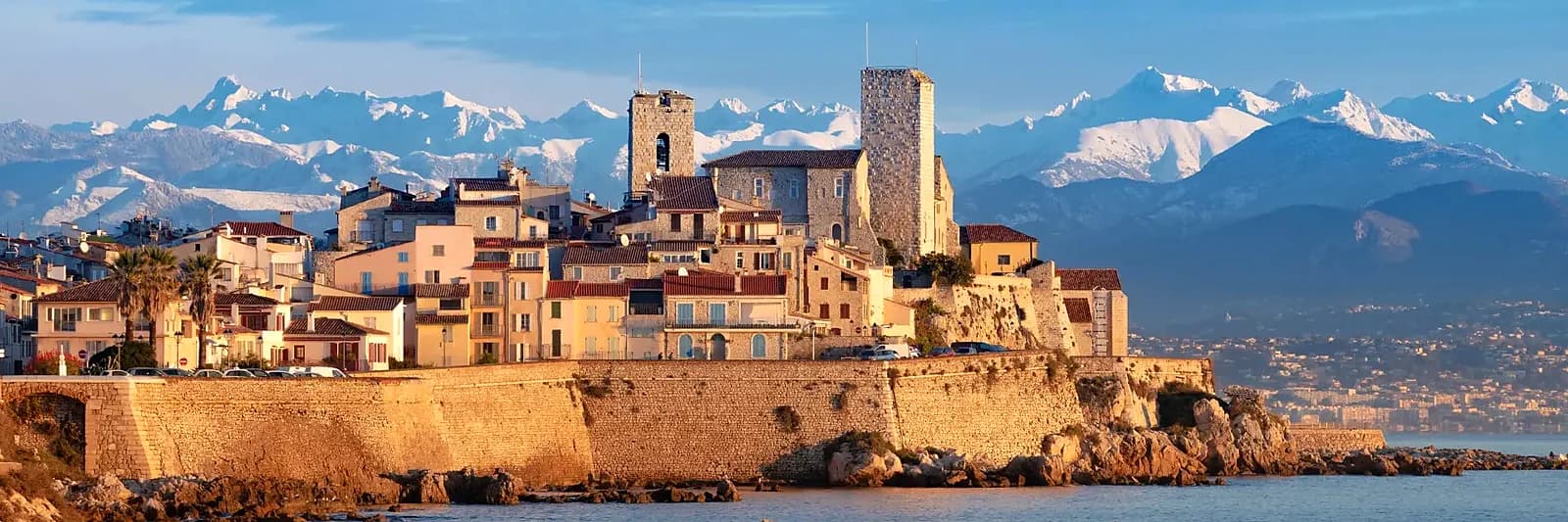 The ramparts of Old Antibes and the Château Grimaldi at golden hour, the snow-capped Alps behind