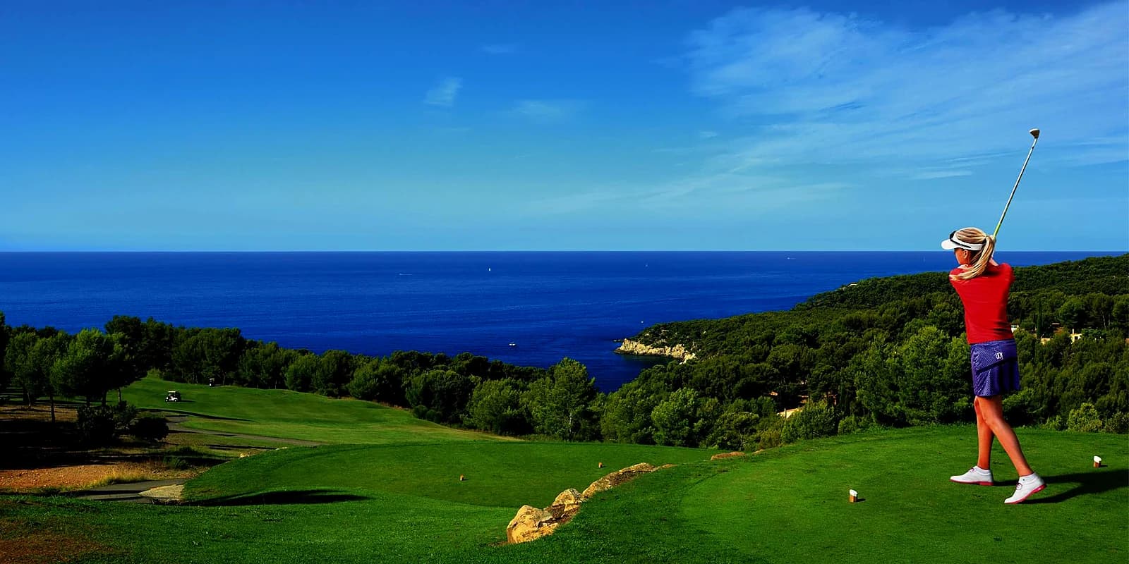 A golfer teeing off above the Mediterranean on a course near Antibes, pines and a blue cove below