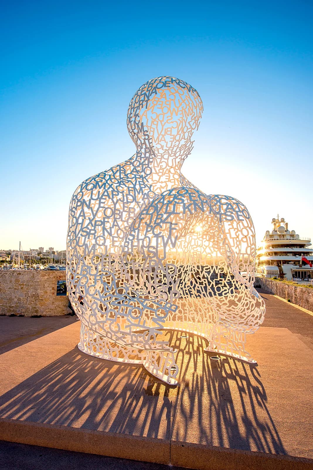 Jaume Plensa’s Nomade on the Saint-Jaume bastion at sunset, a superyacht moored behind