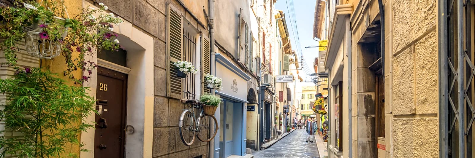 A narrow shopping street in Old Antibes, flowers and shopfronts along the stone façades